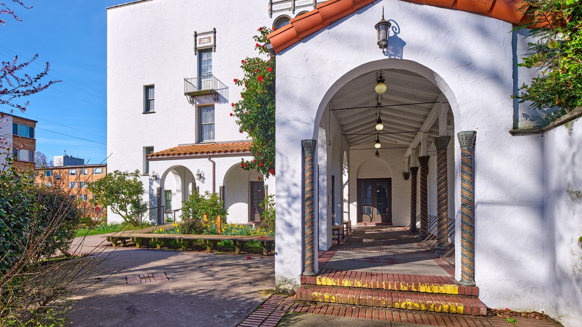CornishKerryHall_Outside_02-16-9-2000x1125 Spanish colonial style building with archways and tiled pillars, bright sunny day, site of a recent sit-in protest, residential area in background.